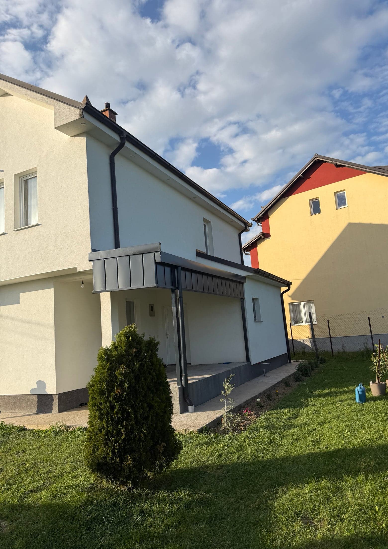 Shtëpi me strehë hyrjeje të veshur me llamarinë ngjyrë antracit, me ulluqe dhe gypa vertikalë në ngjyrë të errët